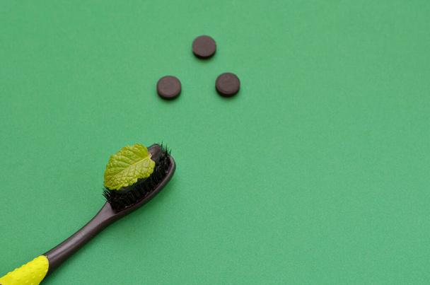 pasta de dientes negro con carbón vegetal en el cepillo de dientes y hoja de menta sobre fondo verde, espacio para copiar - Foto, Imagen