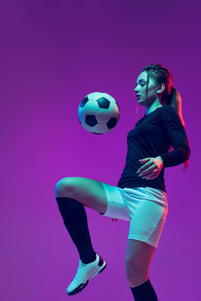In action. One sportive girl, female soccer player training with football ball isolated on purple studio background in neon light. Sport, action, motion, fitness - Фото, зображення