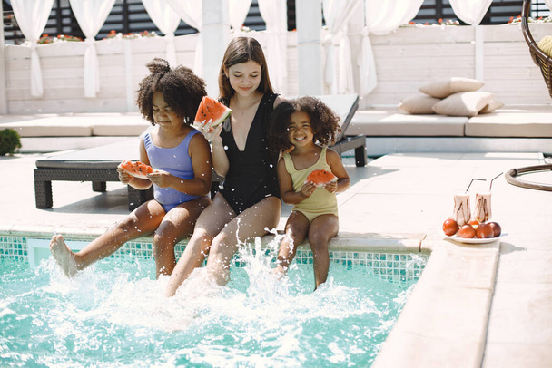 Two african american daughter and their caucasian mother sitting near the pool - Fotoğraf, Görsel