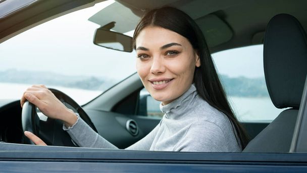 Fiatal női sofőr ül egy autóban, és a kamerába néz - Fotó, kép