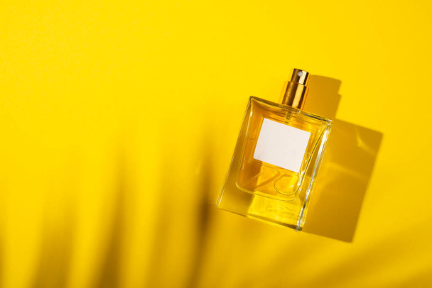 Transparante fles parfum met etiket op gele achtergrond. Parfumpresentatie met daglicht. Trending concept in natuurlijke materialen met mooie schaduw. De essentie van vrouwen. - Foto, afbeelding