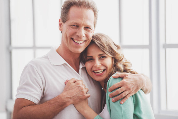 Portrait of happy beautiful couple in casual clothes cuddling, looking at camera and smiling - Photo, Image