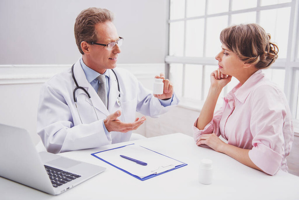 Attractive woman on consultation.  Handsome middle aged doctor is offering medicine - Photo, image