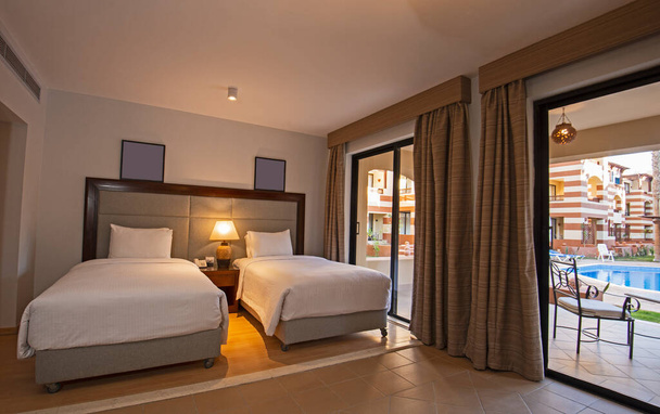 Camas individuales en suite de una habitación de hotel de lujo con terraza y vista a la piscina - Foto, Imagen