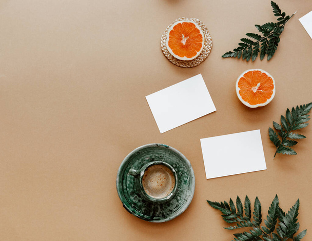 Blank paper card and a cup of coffee. Minimalist concept with oranges and green leaves.  Mock up or template, copy space, flat lay. - Zdjęcie, obraz
