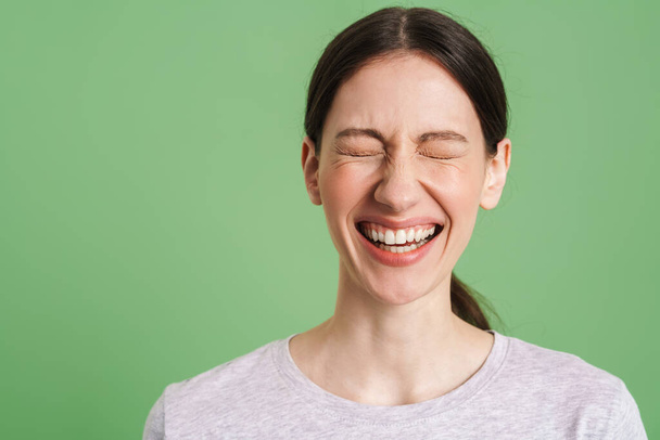 Young brunette woman laughing with her eyes closed isolated over green background - 写真・画像