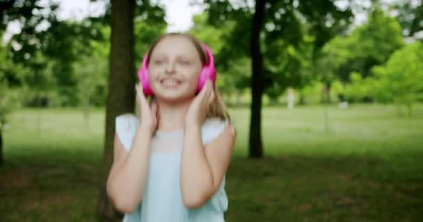 Szczęśliwe dziecko dziewczyna w słuchawki taniec i skoków podczas słuchania muzyki - Materiał filmowy, wideo