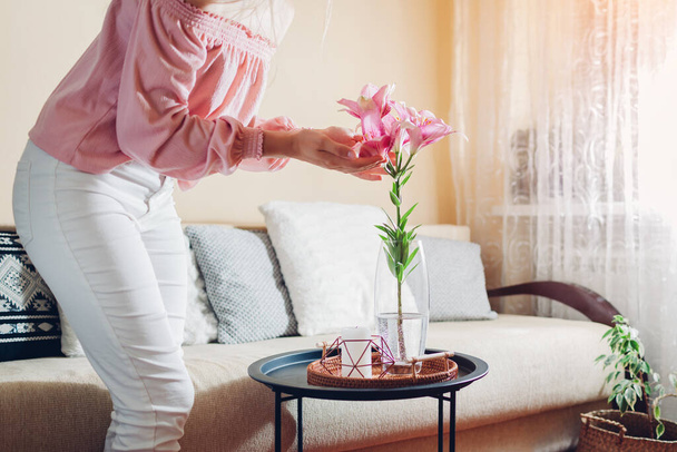 Donna godendo fiori di giglio in vaso a casa. Giovane casalinga ammira bouquet di fiori freschi. Interno e arredamento del soggiorno - Foto, immagini