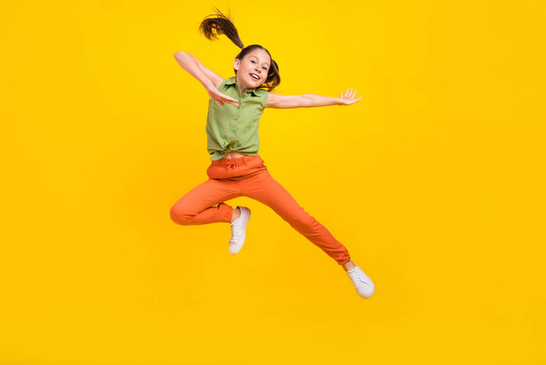 Photo of cheerful excited preteen girl dressed green top jumping high dancing smiling isolated yellow color background - Фото, изображение