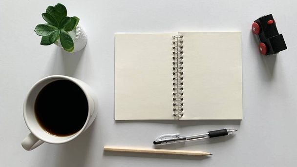 Bovenaanzicht van blanco notitieblok, pen en koffie met witte achtergrond. - Foto, afbeelding