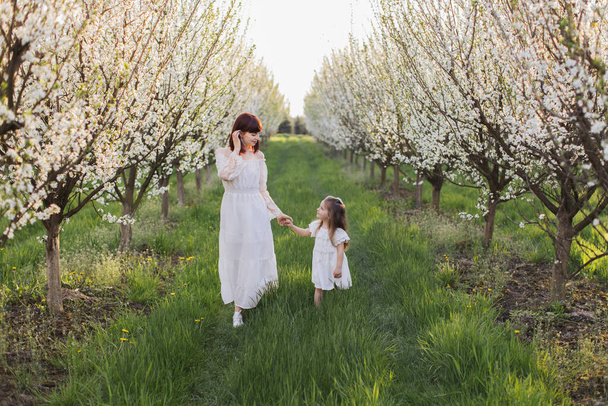 Mother and daughter in white dresse walking at spring garden - Photo, image