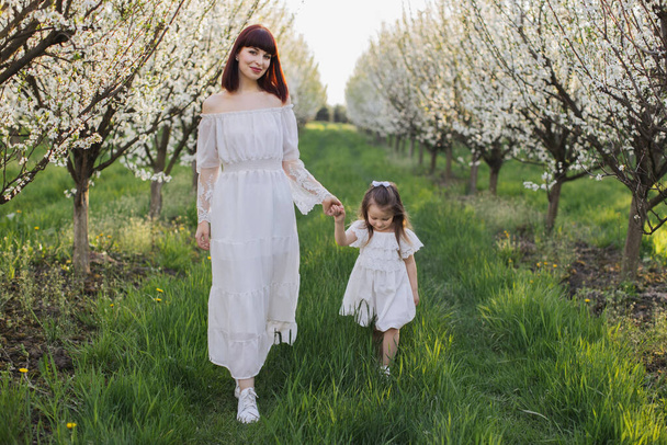 Mother with daughter walking at blooming spring garden - Foto, afbeelding