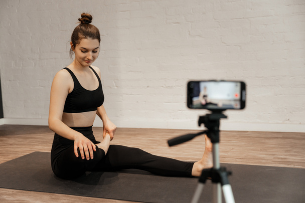 fitness woman make stretching exercises in front camera on tripod at home. - Φωτογραφία, εικόνα