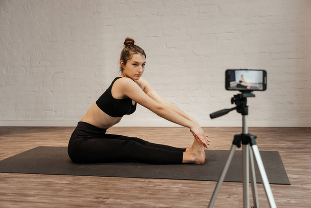 fitness woman make stretching exercises in front camera on tripod at home. - Photo, Image