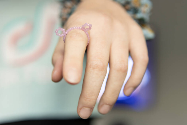 niños mano primer plano en el dedo un anillo con cuentas de color rosa - Foto, imagen