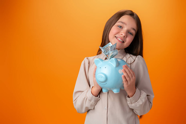 Teen girl with piggy bank on orange color background. - Foto, immagini