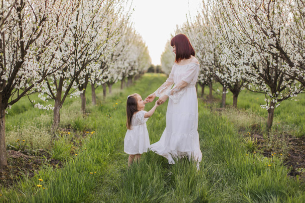 Lovely mother playing with daughter among blooming garden - Zdjęcie, obraz