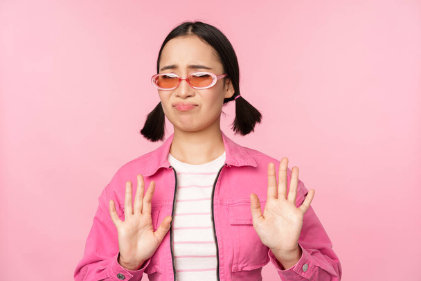 Kösz, nem. Undorodó ázsiai lány napszemüvegben, elutasító smth, kezet rázva, hogy megtagadja, hanyatlás, álló felett rózsaszín háttér - Fotó, kép