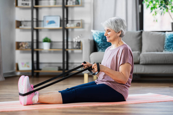 senior woman exercising with elastic band at home - Foto, afbeelding
