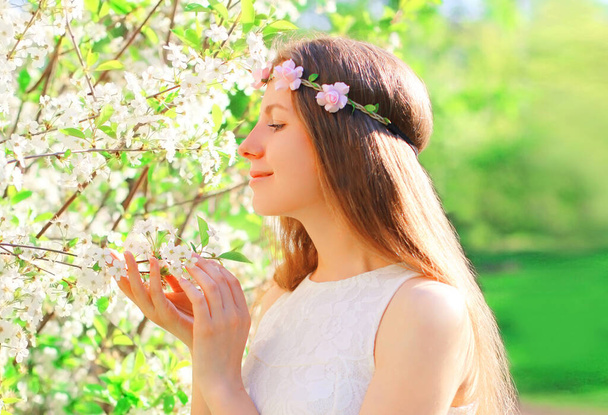 Portrait of beautiful cute young woman and petals of flowers white tree wearing floral headband in spring blooming garden - Foto, Imagen