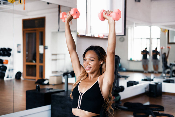 An African-American coach is engaged in body stretching in the gym. A healthy lifestyle. Useful loads on the body's cardiac system. A strong, confident woman does exercises in a fitness club. - Foto, Imagem