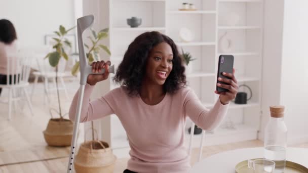 Счастливая африканская женщина с костылями Видео Звонок с помощью смартфона в помещении - Кадры, видео