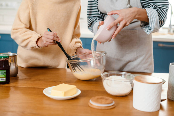 Caucasian beautiful mother and daughter making pancake dough in cozy kitchen - Fotó, kép