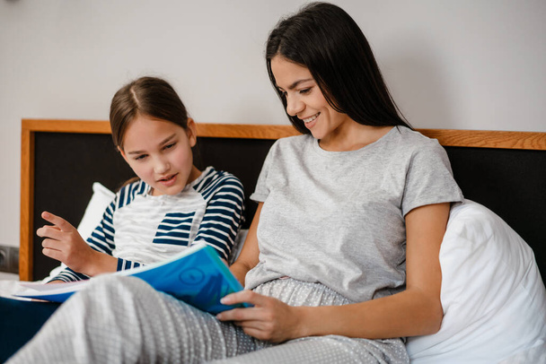 Happy mother and daughter doing homework while laying on bed indoors - Foto, Imagen