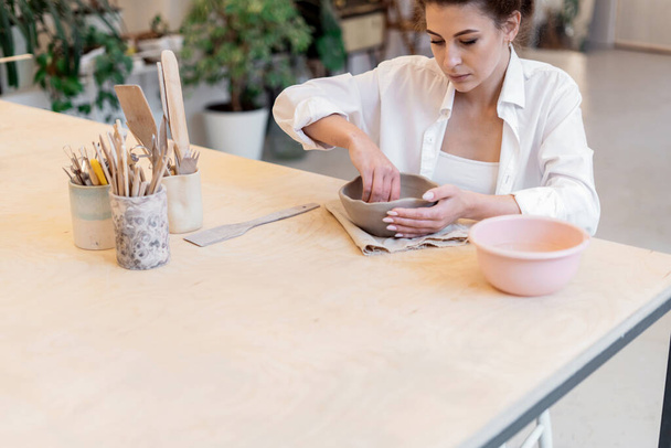 Clay and porcelain dishes to order. Ceramist woman in the workshop. Individual products for the home. Master in the ceramics studio. Uniform for convenient and comfortable work. - 写真・画像