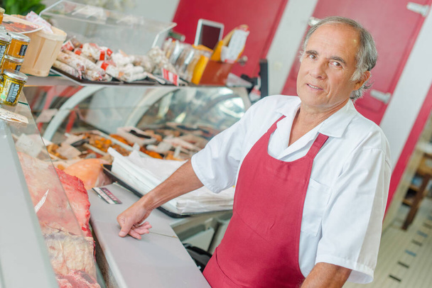 a butcher standing behind counter - Foto, afbeelding