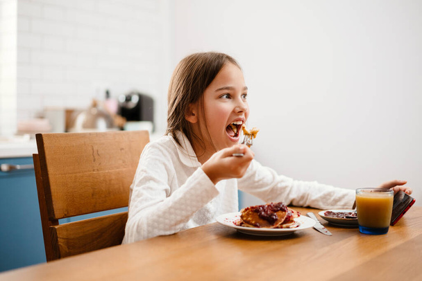 Little girl sitting at the table and eating pancakes in the kitchen - Photo, Image