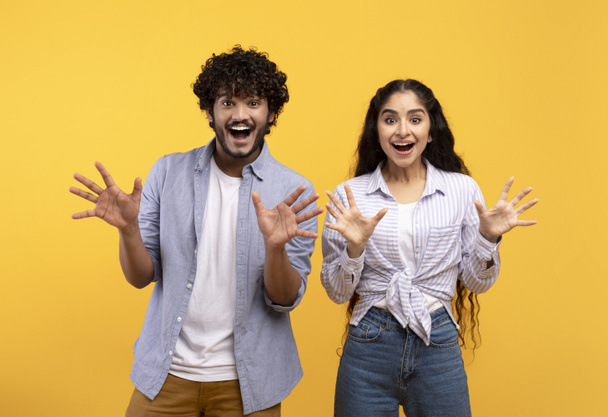 Συναισθηματική ινδική ζευγάρι gesturing μαζί, έχοντας έκπληξη εκφράσεις του προσώπου και δείχνει έκπληξη, κίτρινο φόντο - Φωτογραφία, εικόνα