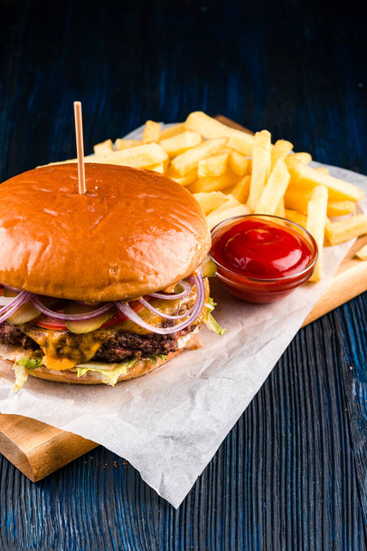 Close up of gourmet pub hamburger with bacon on wooden table, large burger with potatoes and ketchup close-up, big burger and some french fries - Fotó, kép