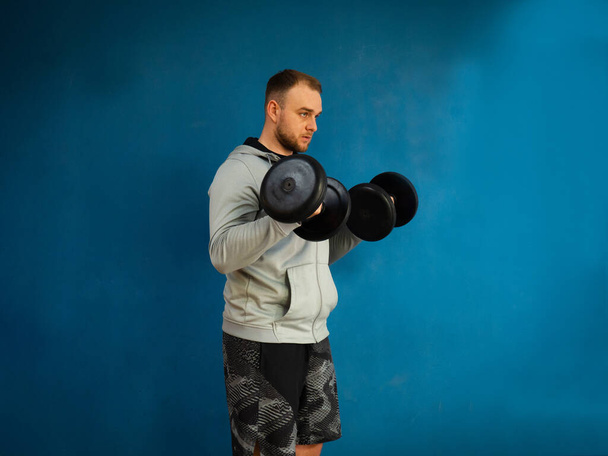 Молодой активный мужчина тренирует мышцы бицепса с тяжелым гантели весом в тренажерном зале - Фото, изображение