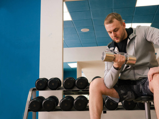 Schweres Krafttraining. Bodybuilder trainiert mit Kurzhanteln im Fitnessstudio, leerer Raum - Foto, Bild