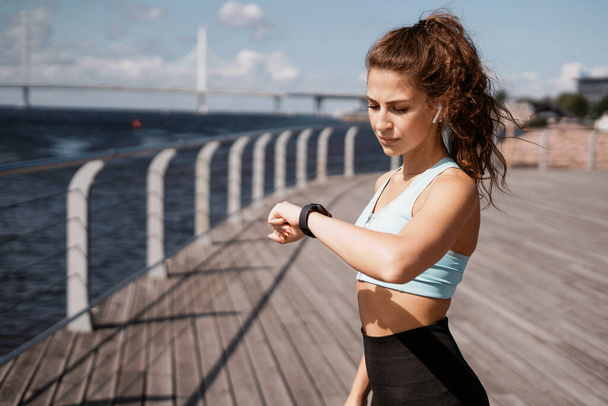 Portrait of a woman exercising and running. Smart watch heart rate measurement. The trainer is a marathon for a distance. Fitness cardio workout on the street in the city. Health and lifestyle. - Foto, Bild