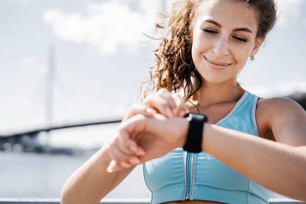 The calorie counting coach looks at the smartwatch. Fitness break in the city. The athlete leads a healthy lifestyle. Cardio training for weight loss. Sports and clothing for women. - Foto, Bild