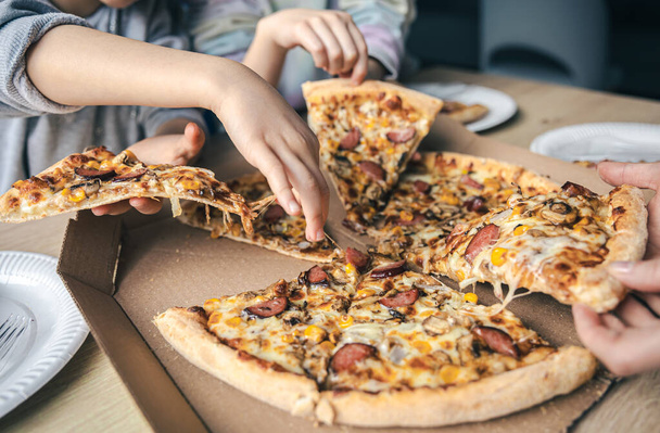 Jugendliche holen am Tisch heiße Pizza aus Pappschachtel. - Foto, Bild