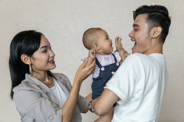 Familienmoment: Junges malaiisches Paar mit Kleinkind lächelt einander zu - Foto, Bild