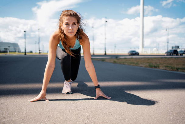 A confident brunette woman leads a healthy lifestyle. The coach trains on the street in the city. The athlete prepares for running, does a warm-up stretching of her body. - Foto, imagen