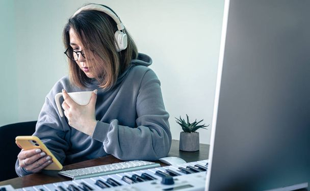 Młoda kobieta tworzy muzykę za pomocą klawiatury muzycznej i komputera. - Zdjęcie, obraz