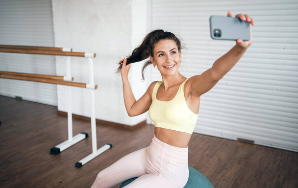 Uses the phone. A confident woman does sports in a club.  Healthy lifestyle and strength training. Coach and work in the fitness room. - Zdjęcie, obraz