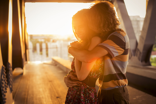 Молода пара обіймається спалахами світла заходу сонця на мосту c
 - Фото, зображення