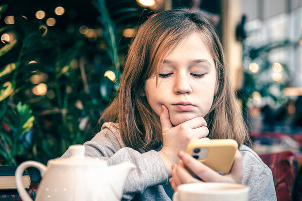 Egy kislány figyelmesen néz az okostelefon képernyőjére. - Fotó, kép