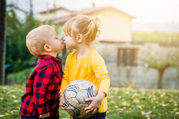 Liebenswert glückliche Kinder im Freien bei Sonnenuntergang - Kleiner Junge küsst ein Mädchen auf dem Spielfeld - Konzept der Liebe und Freundschaft - Foto, Bild