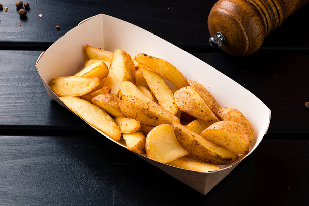 potato slices in a food delivery box. Rustic style golden crispy fried potato wedges sprinkled in box. Takeaway food in fast food restaurant - Photo, Image