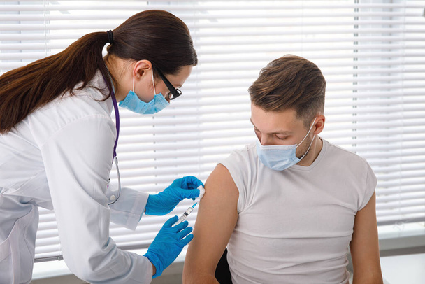 El médico sostiene una jeringa antes de administrarle una inyección a un paciente con una máscara médica. Vacuna contra Covid-19 o coronavirus. Vacunación del concepto de población. - Foto, Imagen