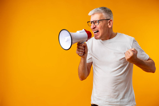 Portrait of mature man shouting with megaphone against yellow background - Photo, Image