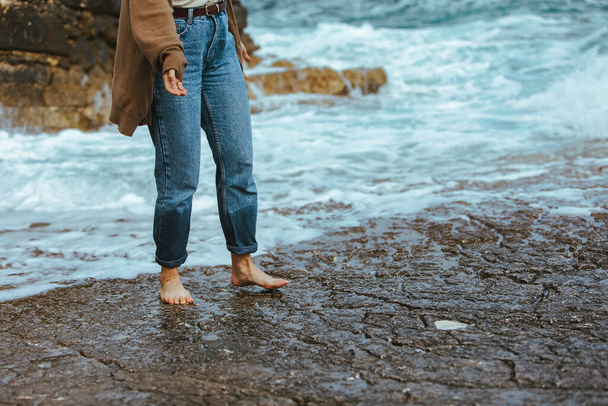 Žena, která chodí po skalnaté pláži bosá džíny letní prázdniny - Fotografie, Obrázek
