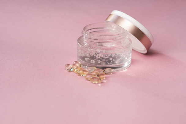 Gel con ácido hialurónico en un frasco de vidrio y cápsulas sobre fondo rosa - Foto, imagen